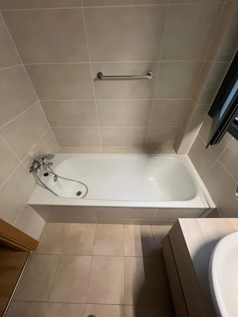 Baño antes de la reforma: bañera con alicatado beige y barra de apoyo