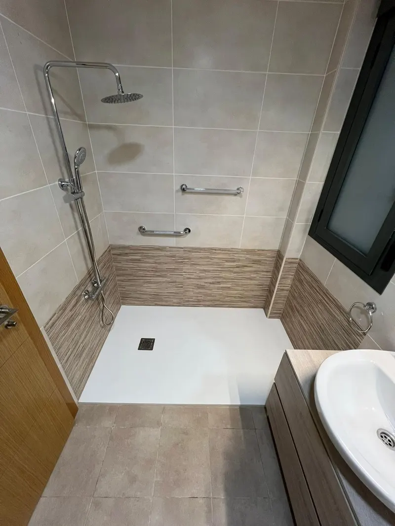 Baño después de la reforma: plato de ducha blanco con alicatado a media altura efecto madera y ducha de lluvia
