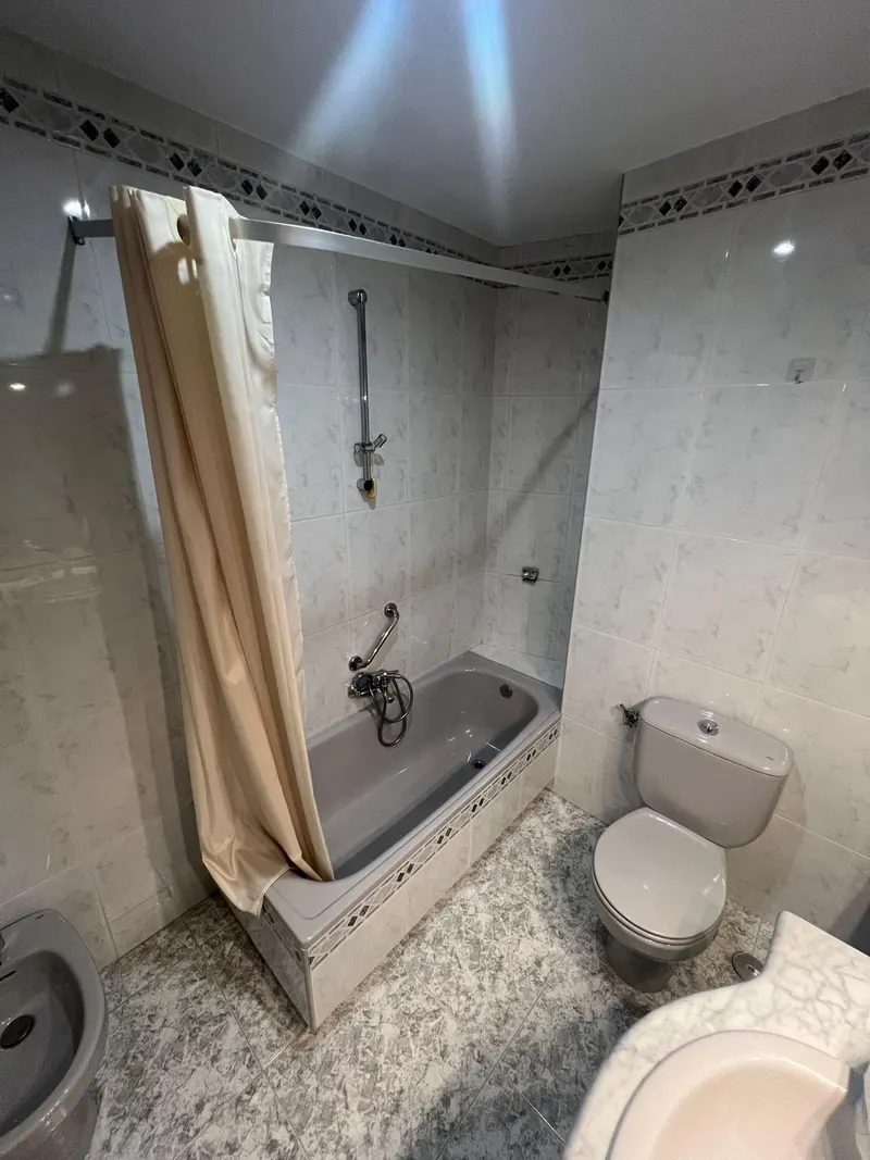 Baño antes de la reforma: bañera gris con cortina