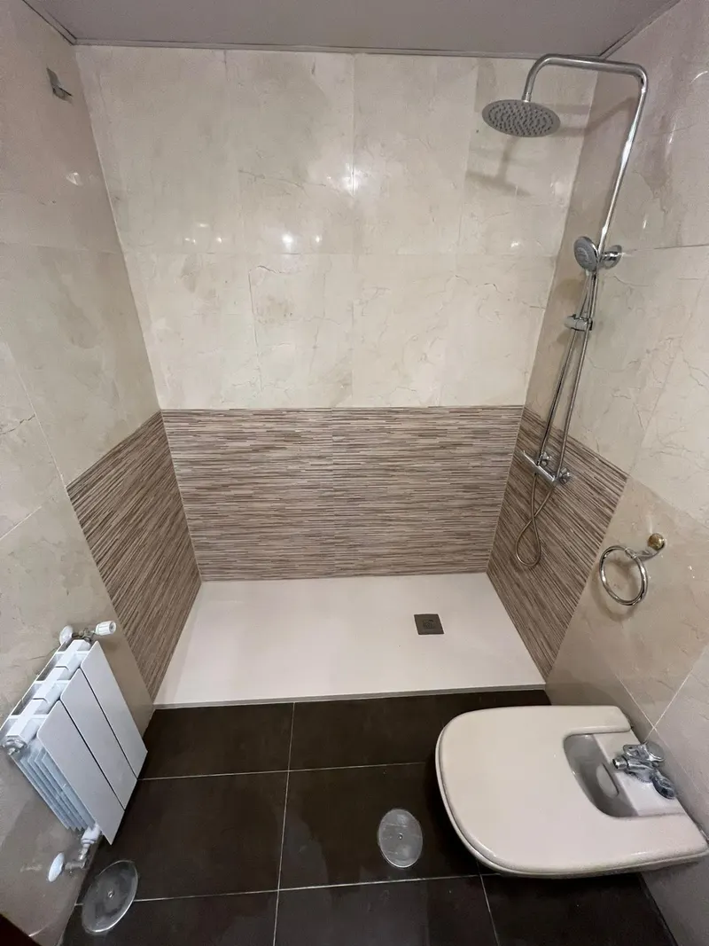 Baño después de la reforma: plato de ducha blanco con alicatado a media altura y ducha de lluvia