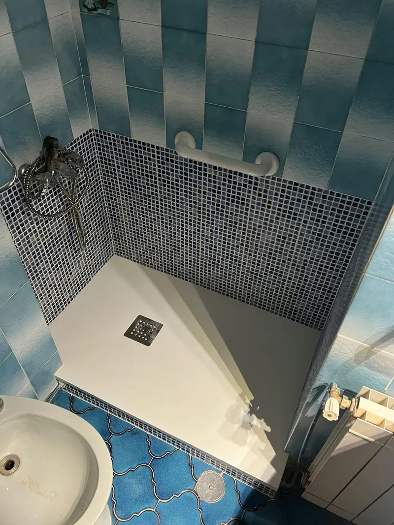 Baño después de la reforma: plato de ducha blanco con mosaico azul y barra de apoyo